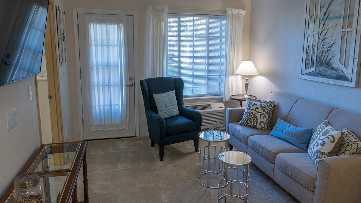 Cozy living room with a chair, sofa, and lamp by the window.