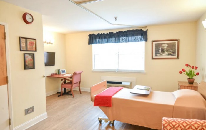 A well-lit room with a bed, desk, and television.