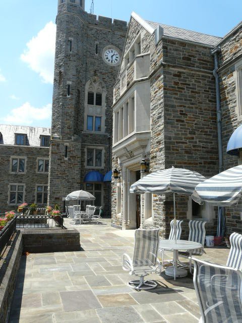 A stone building with a clock tower, featuring outdoor seating with tables and striped umbrellas.