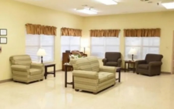 A cozy living room with multiple chairs and sofas, illuminated by table lamps near large windows.