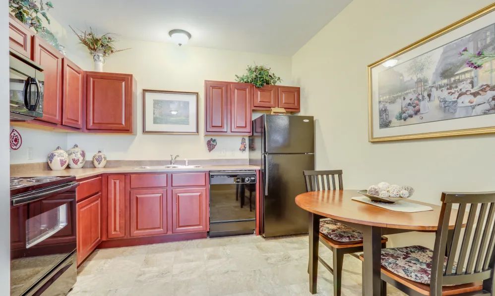 A compact kitchen and dining area featuring red cabinets, a refrigerator, and a small table with chairs.