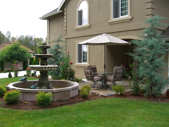 A serene patio with a fountain and outdoor seating in a well-landscaped garden.