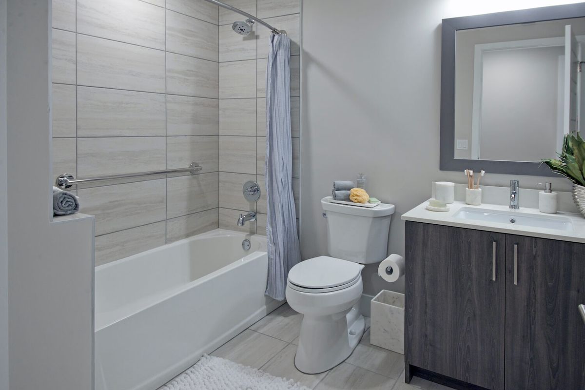 A modern bathroom featuring a bathtub with a shower curtain, toilet, and sink with a mirror.
