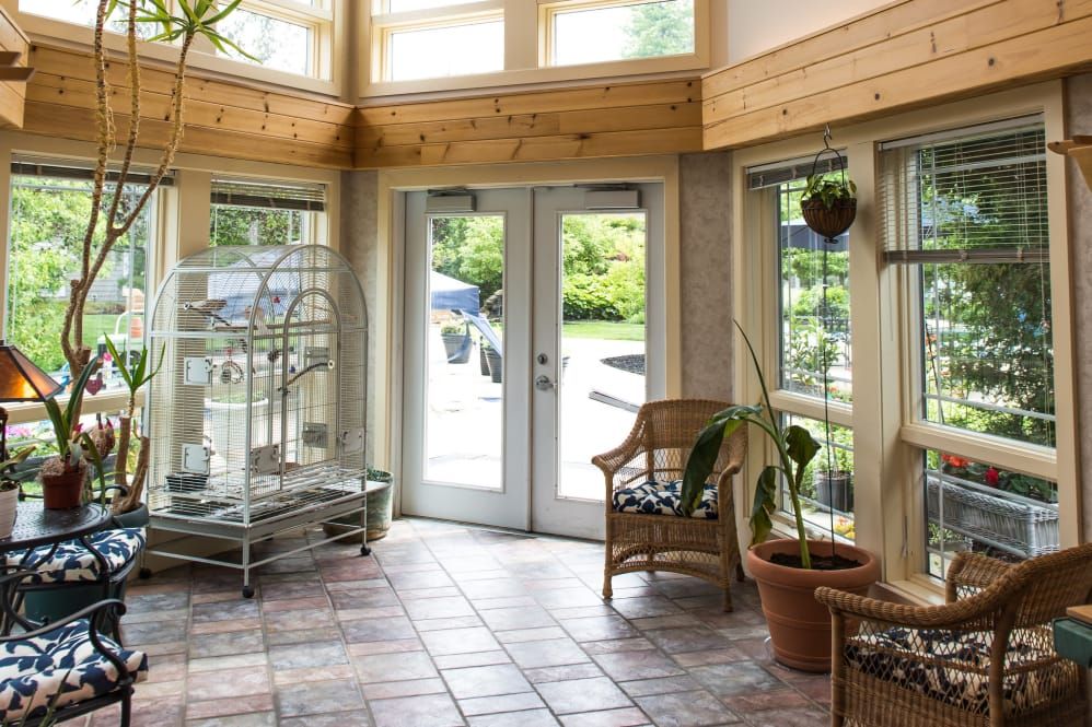 A bright sunroom with French doors, plants, and a cozy chair, filled with natural light.