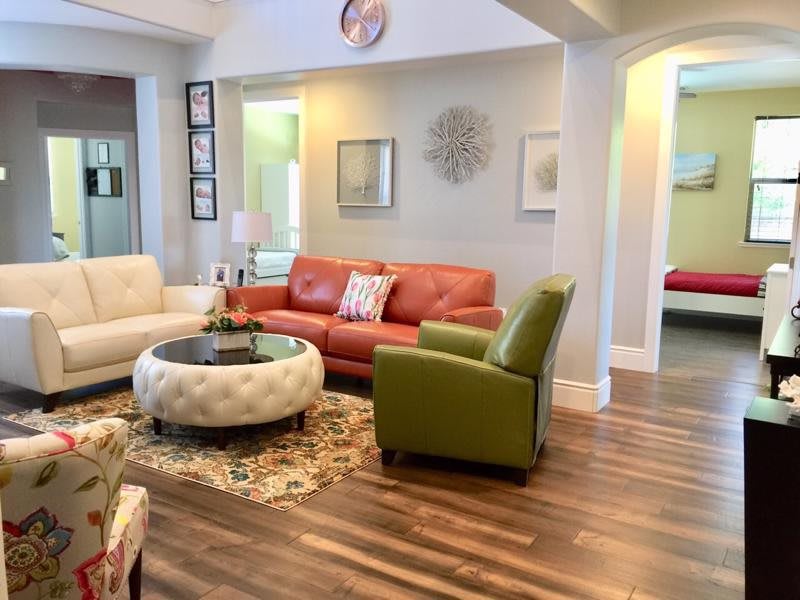 A cozy living room featuring a red couch, green armchair, and tufted coffee table on a decorative rug with hardwood flooring.