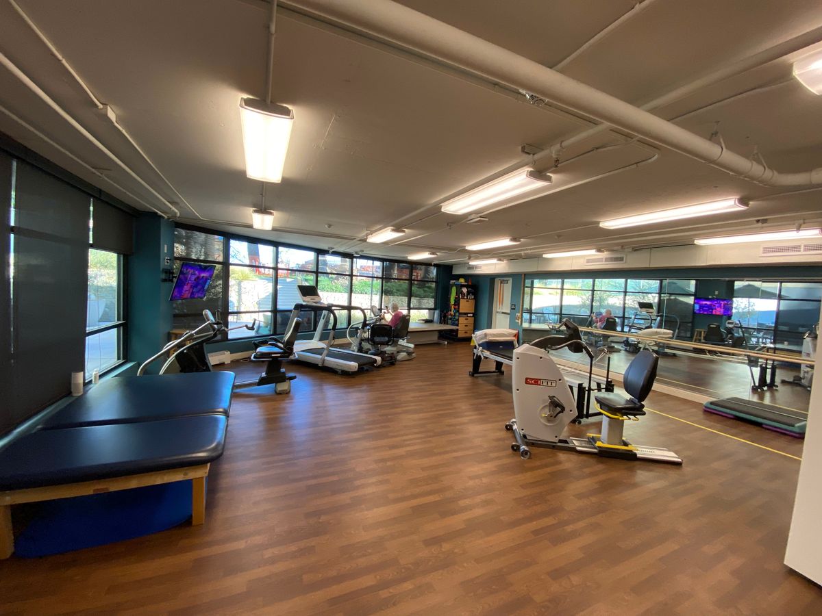 A spacious, well-lit gym with various exercise equipment and large windows.