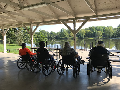 A group of seniors in wheelchairs enjoying the serene view of a lake.