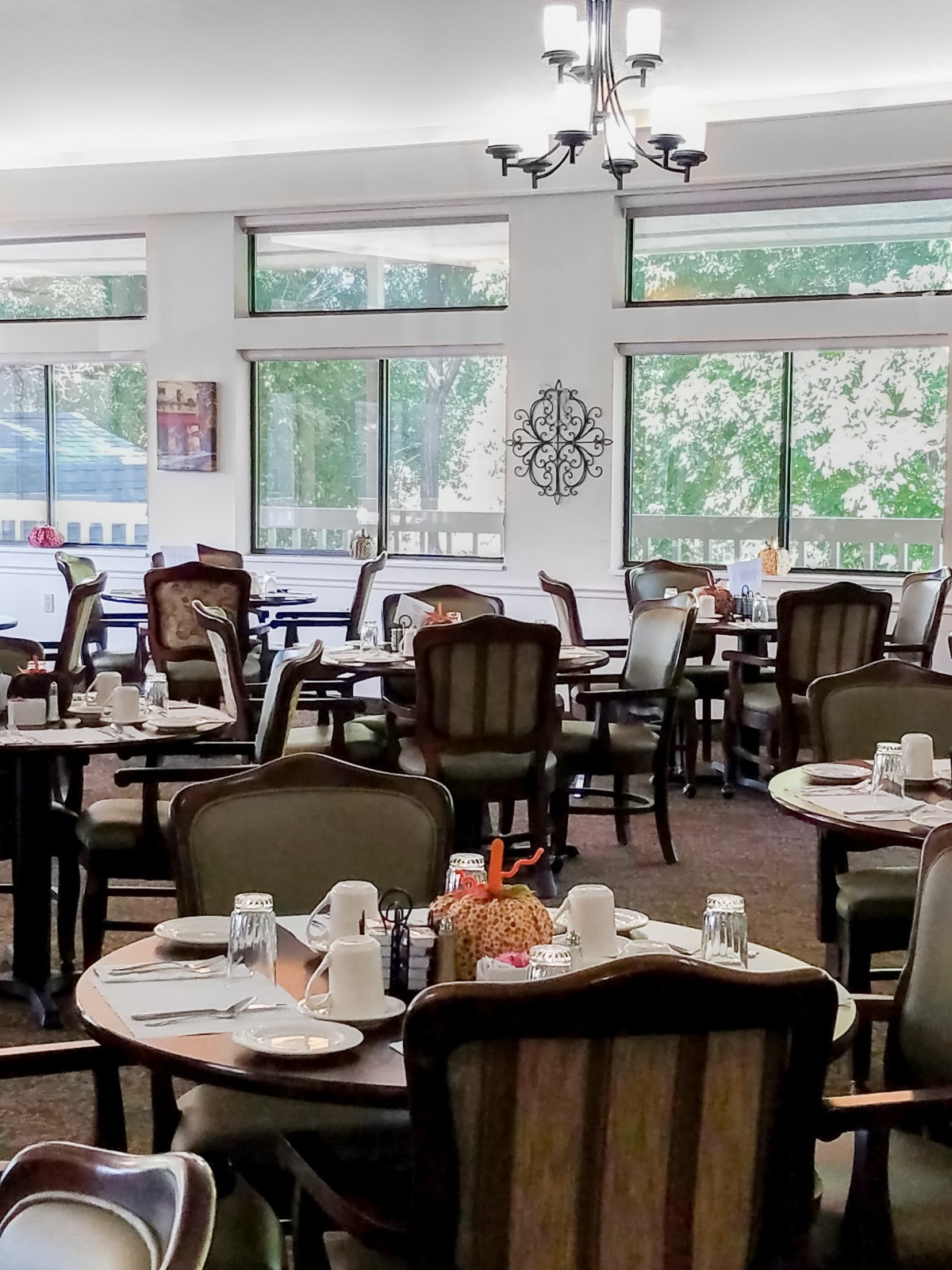 A spacious dining area featuring neatly arranged tables and chairs, set with place settings, surrounded by large windows.