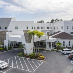 A modern hospital building with a spacious parking lot and palm trees.