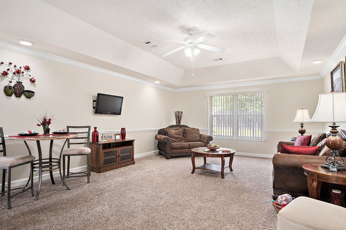 A cozy living room with a sofa and coffee table, featuring a mounted television and ceiling fan.
