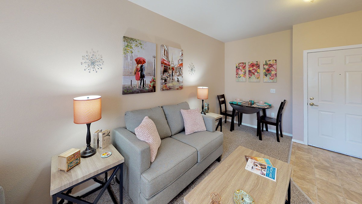 A cozy living room with modern decor featuring a gray sofa, artistic wall pictures, ambient lighting from lamps, and a dining area.