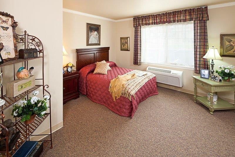 A cozy bedroom with a neatly made bed, a large window, and carpeted flooring.