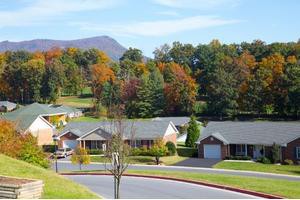 A suburban neighborhood with houses surrounded by autumn-colored trees and mountains in the background.