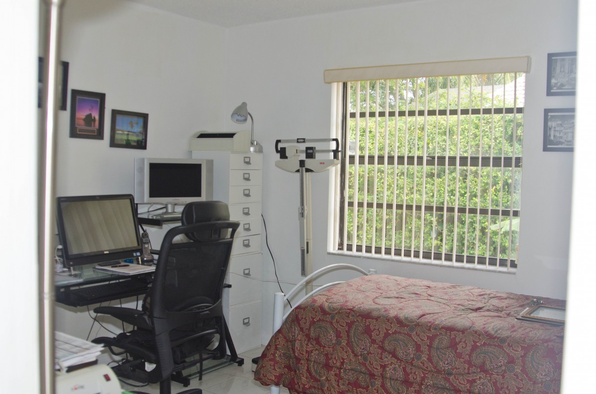 A home office setup in a bedroom with a desk, computer, and bed.