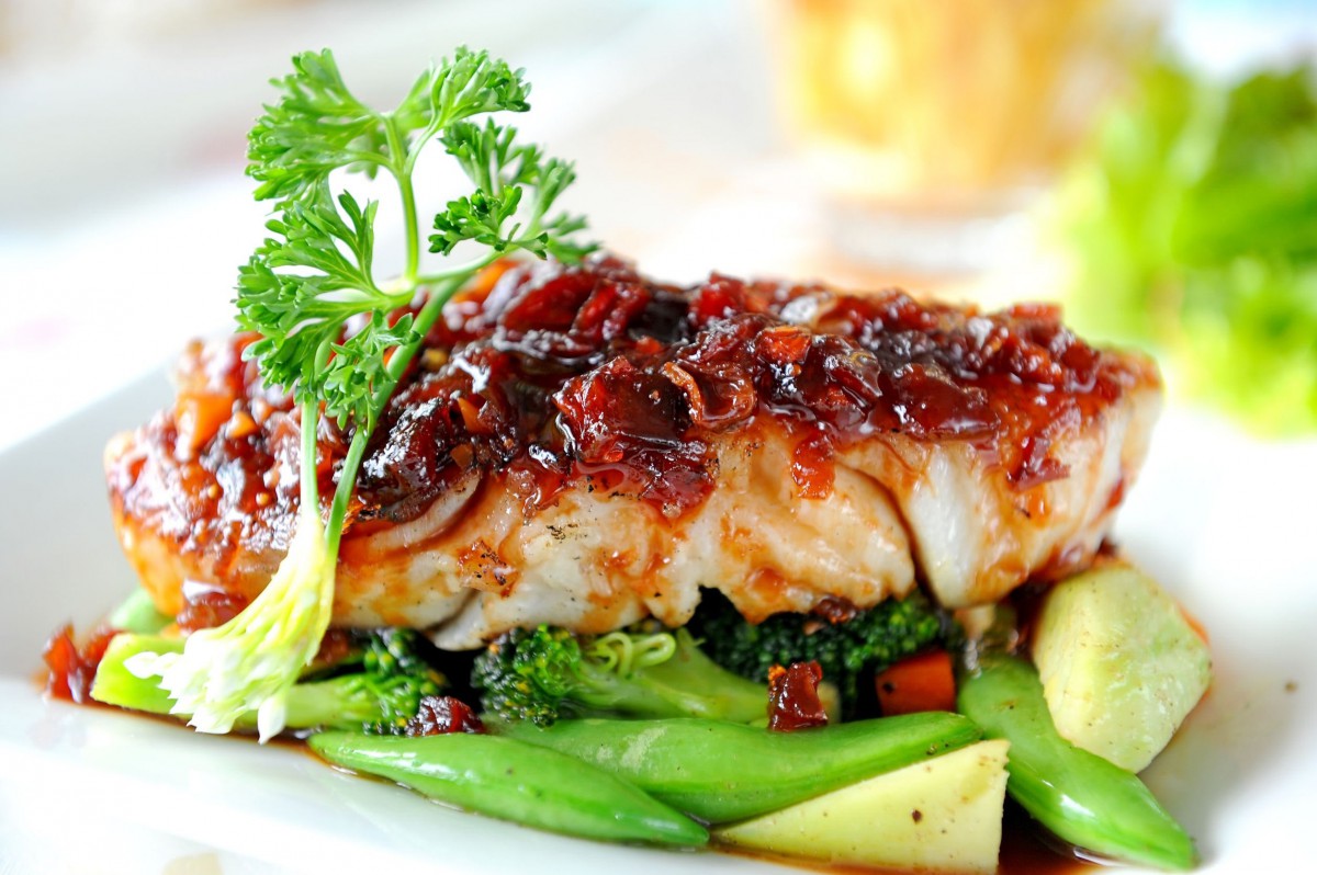 A gourmet fish dish garnished with herbs and served on a bed of mixed vegetables.