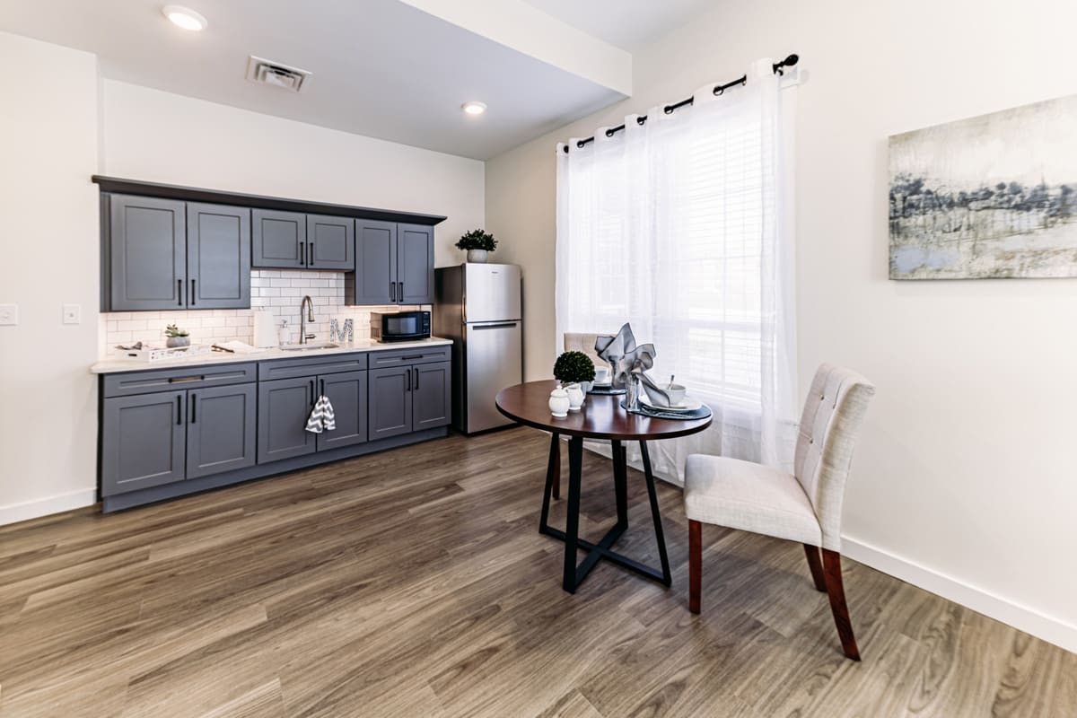 A modern kitchen-dining area with grey cabinets, hardwood floors, and ample natural light.