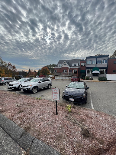A cloudy day at a parking lot with various cars parked in front of a building.