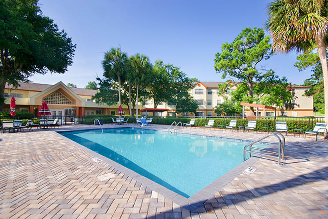 A sunny day at a residential outdoor swimming pool surrounded by trees and buildings.