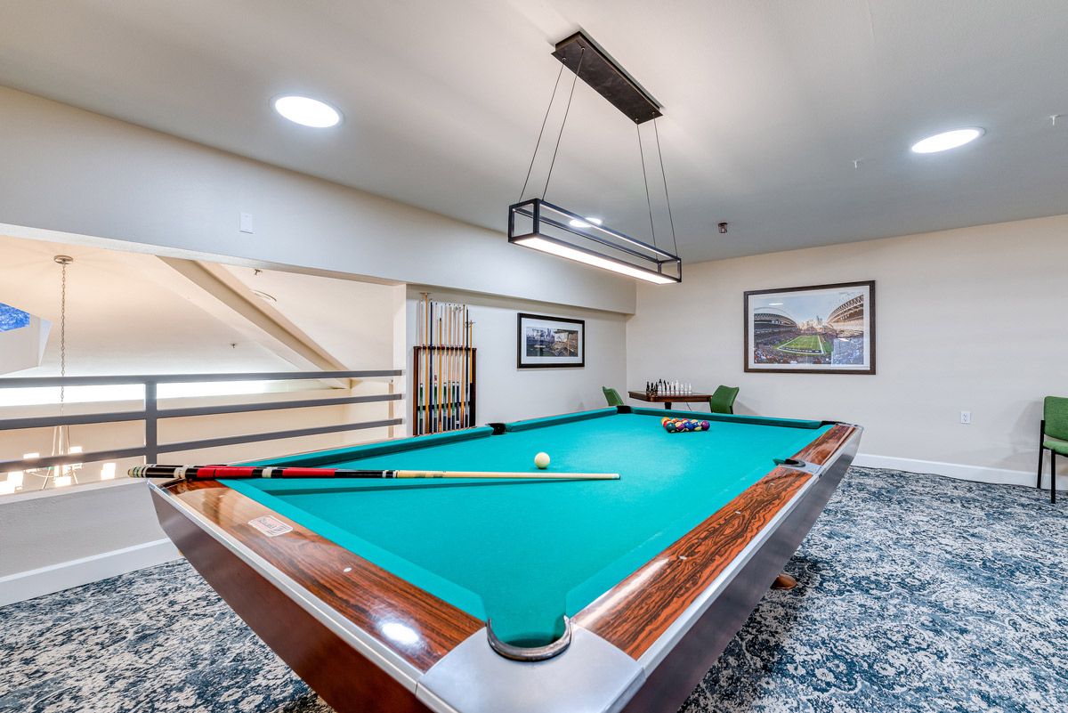 A well-lit recreational room featuring a pool table with cue sticks and balls ready for a game.