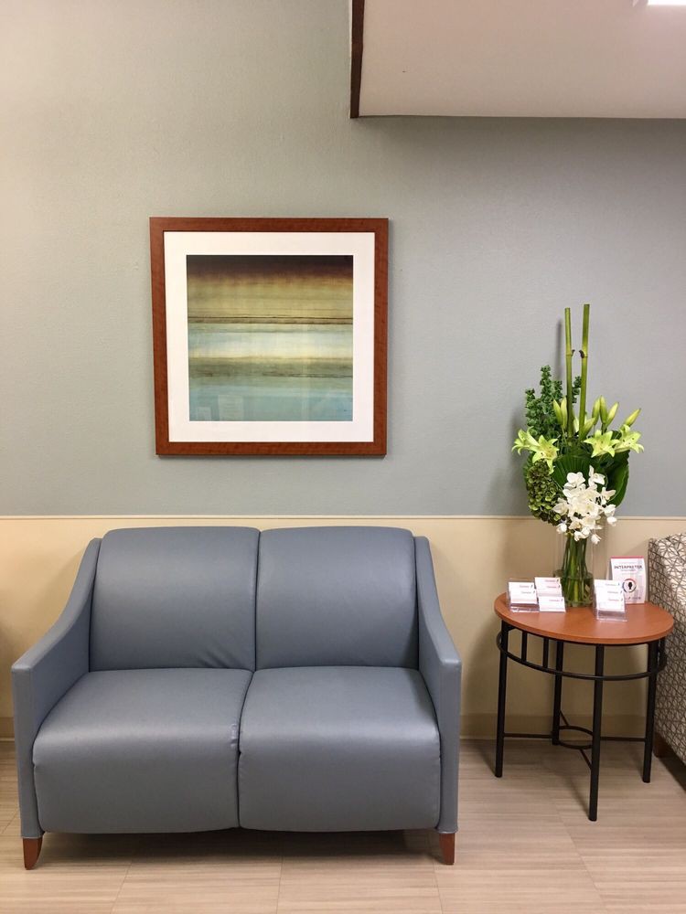 A quiet waiting room with a blue sofa, abstract painting, and a table adorned with flowers.
