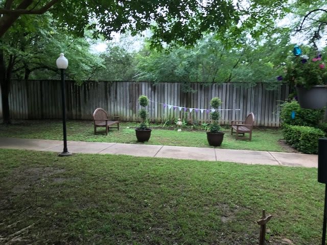 A tranquil garden setting with chairs, neatly trimmed plants, and a lamppost beside a wooden fence.