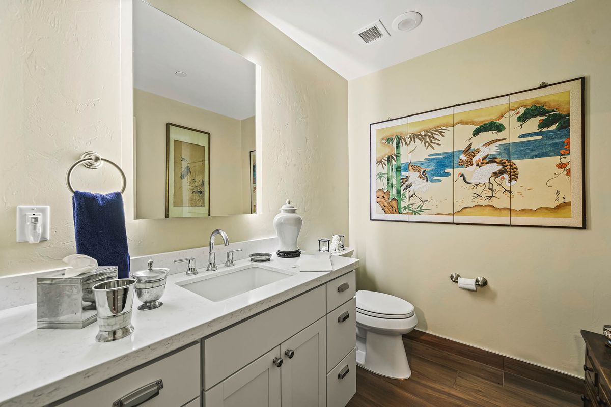 A modern bathroom with a sleek design, featuring a sink area with large mirror, elegant countertop, and stylish wall art.