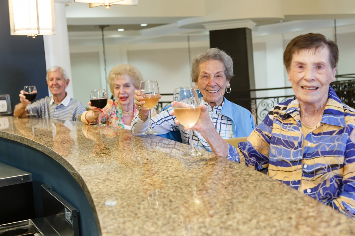 A group of seniors enjoying drinks together at a bar, toasting with smiles.