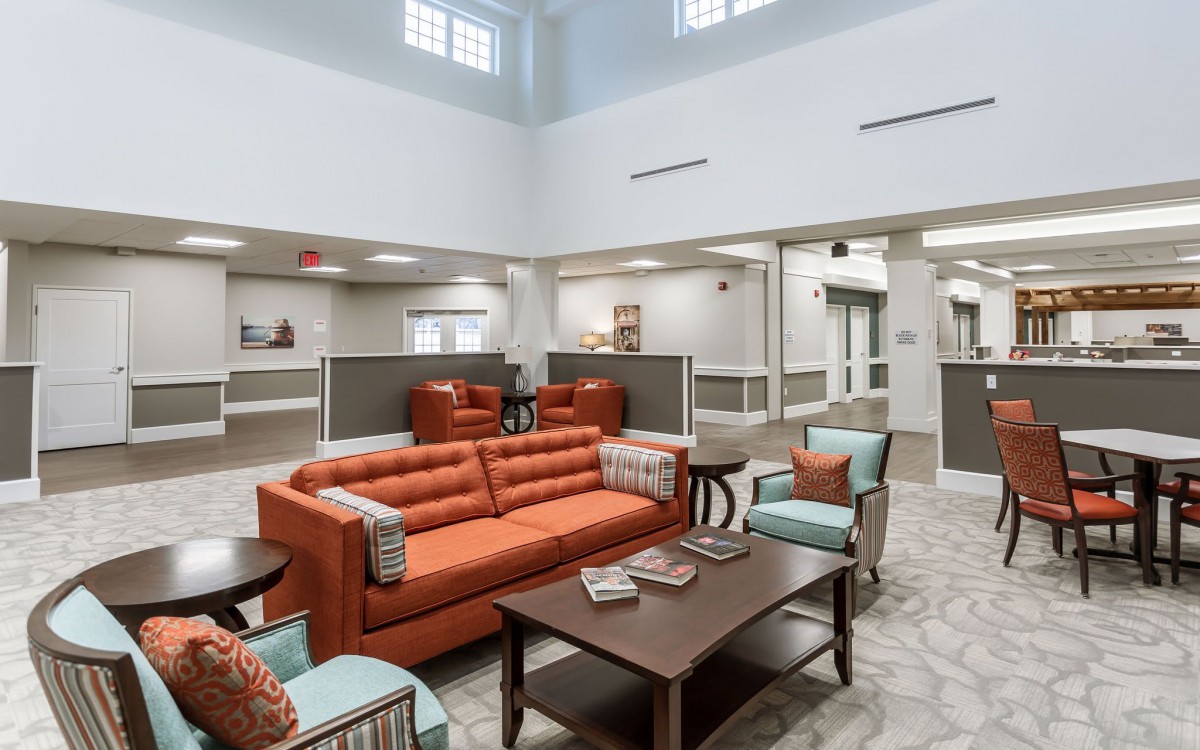 A modern lobby area featuring orange sofas, chairs, and a coffee table in a bright and spacious setting.