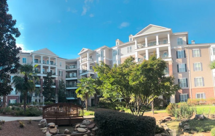 A scenic view of modern apartment buildings surrounded by trees under a clear blue sky.
