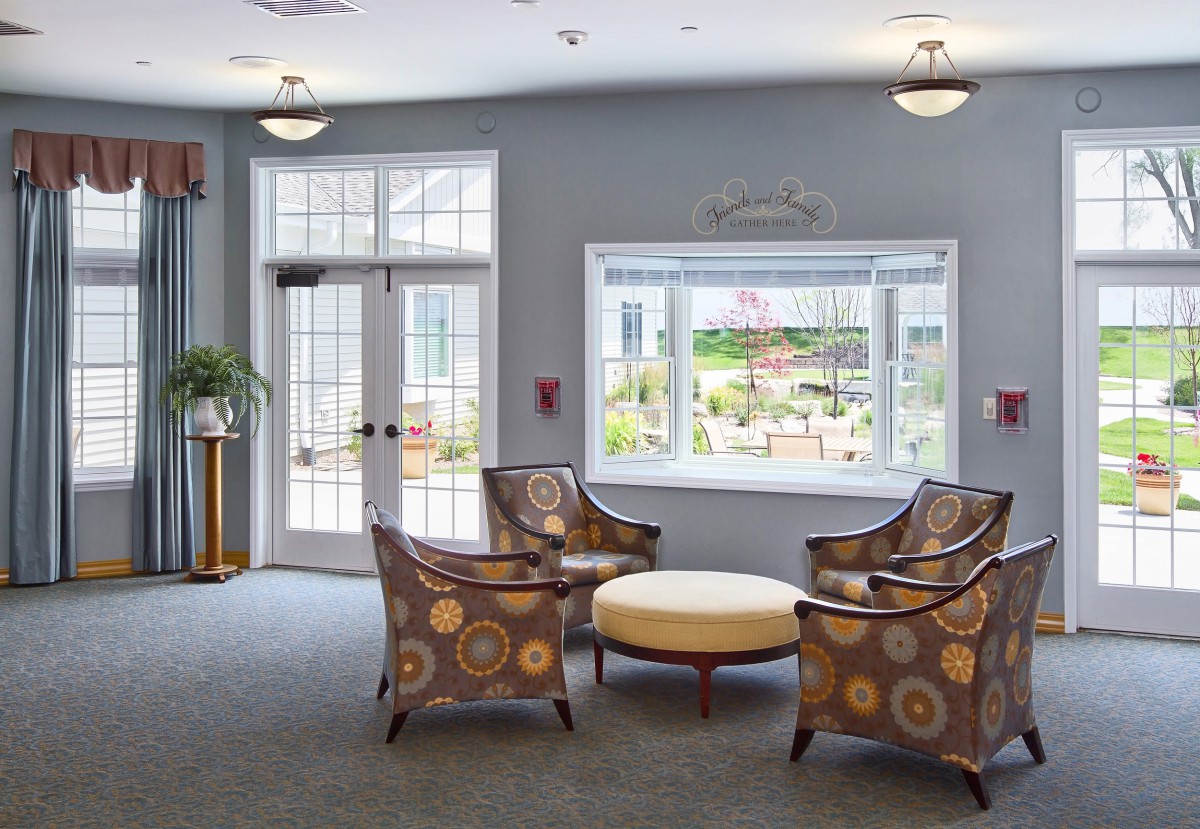 A cozy lobby seating area with patterned chairs and a round table, illuminated by natural light from a large window.