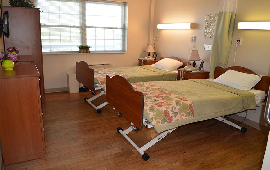 A clean and organized hospital room with two beds, featuring a well-lit space and wood flooring.