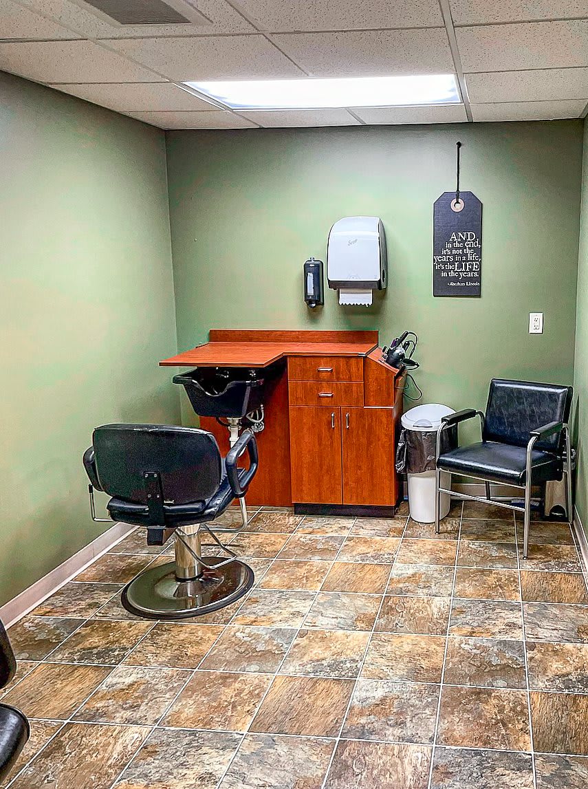 A small hair salon waiting area with a barber chair and a wall-mounted paper towel dispenser.