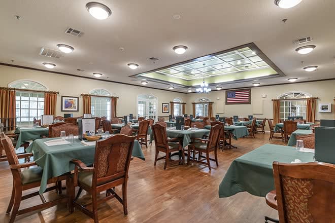 A spacious dining area with neatly arranged tables and chairs, featuring wooden floors and ambient lighting.