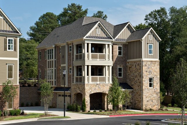 A modern multi-story house with stone exterior and balconies set amidst trees.