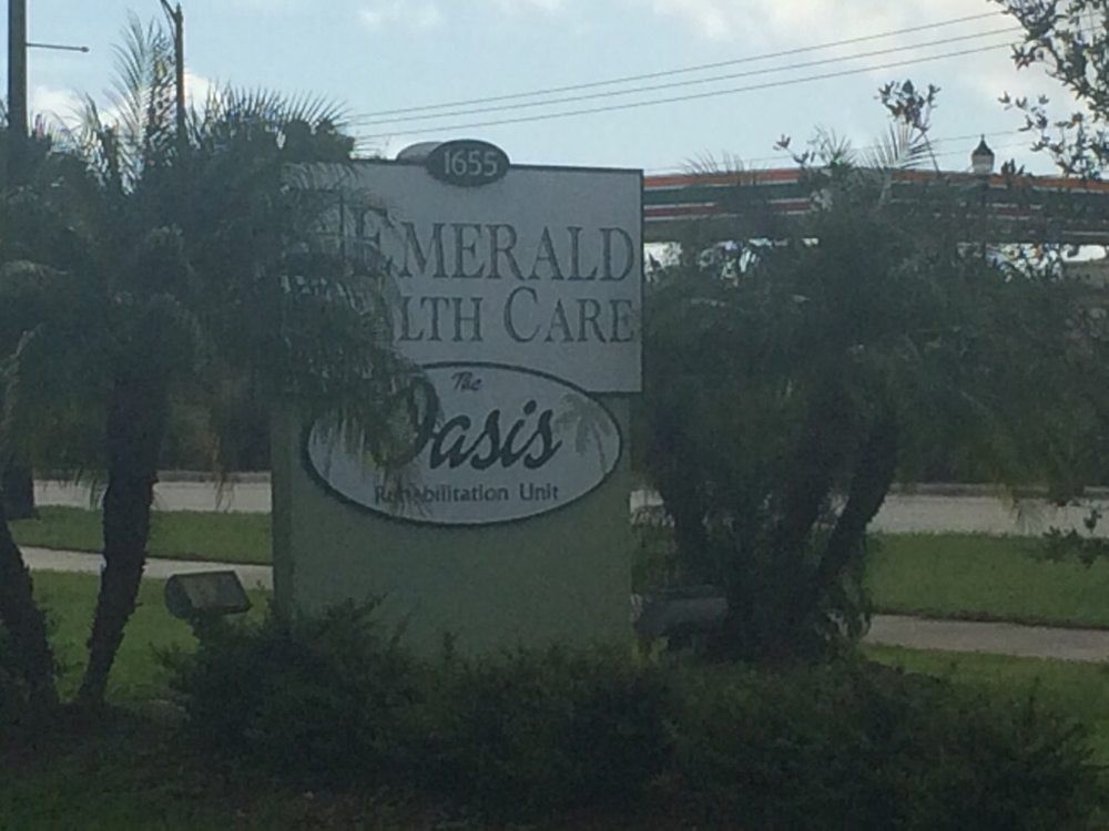 A sign for Emerald Health Care Oasis surrounded by greenery.