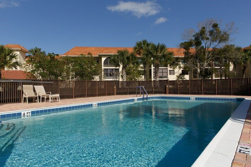 A sunny day by a swimming pool with a building and trees in the background.