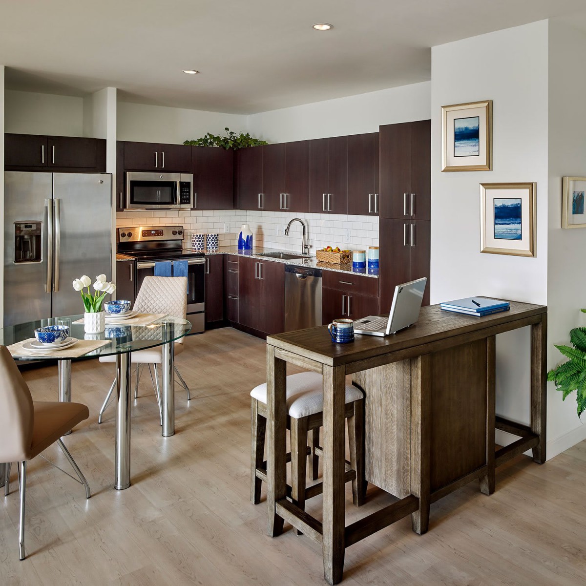 A modern kitchen with stainless steel appliances and a dining area, featuring wood cabinets and stylish decor.
