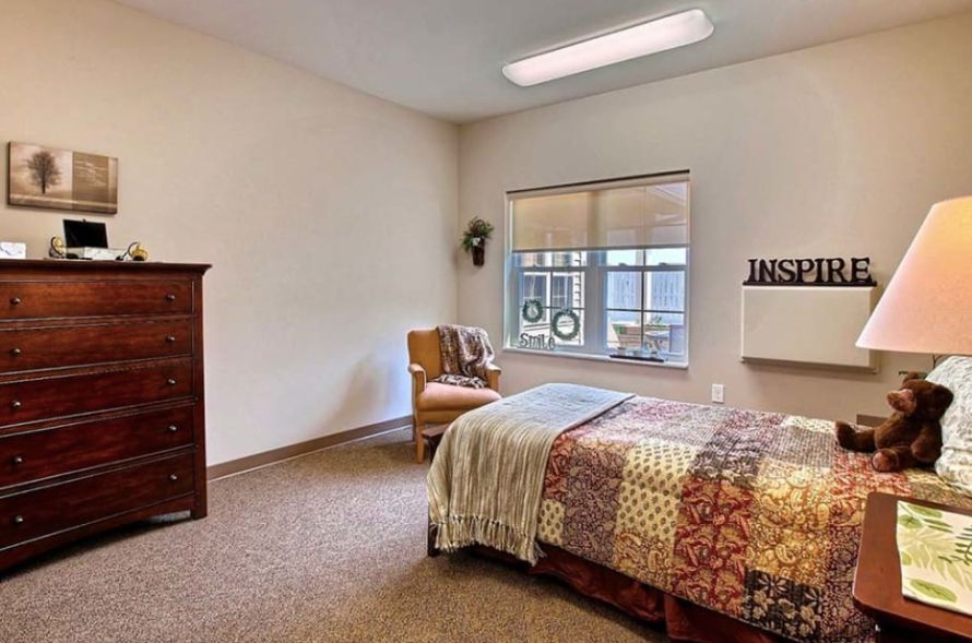 A minimalist bedroom with a single bed, a patterned quilt, and a comfortable chair near the window.
