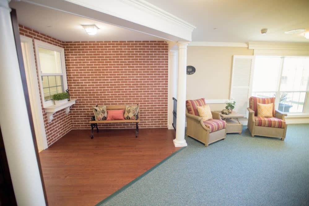 A cozy living room featuring a mix of wood and carpeted floors, with a brick accent wall and comfortable seating.