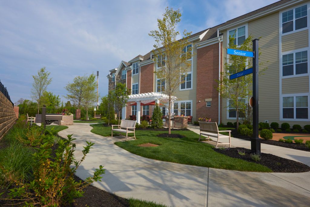 A modern residential building with landscaped gardens and a pathway lined with benches.