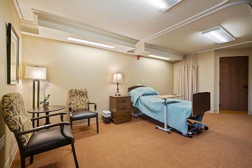 A well-furnished hospital room with a patient bed and comfortable seating areas.