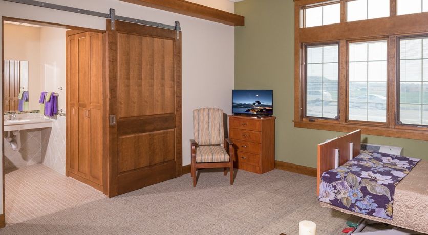 An office space with a wooden chair, a TV on a cabinet, and a sliding wooden door.