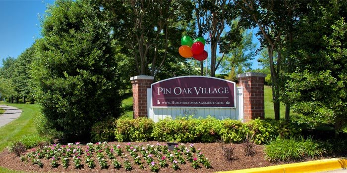 Entrance sign to Pin Oak Village with balloons and well-maintained landscaping.