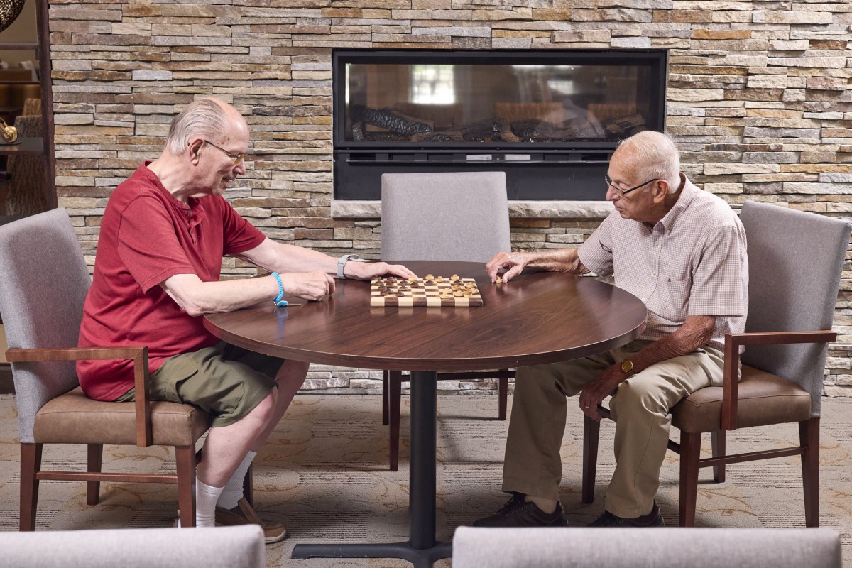 Two elderly men engaged in a game of chess at a round table indoors.