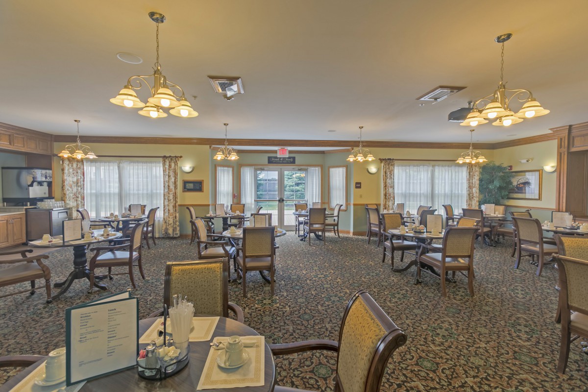 A spacious dining room with neatly arranged tables and chairs, illuminated by elegant lighting fixtures.