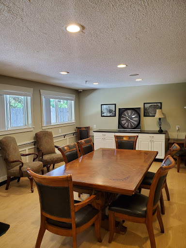 A spacious meeting room featuring a large wooden table surrounded by chairs, with natural light coming from the windows and a dartboard on the wall.
