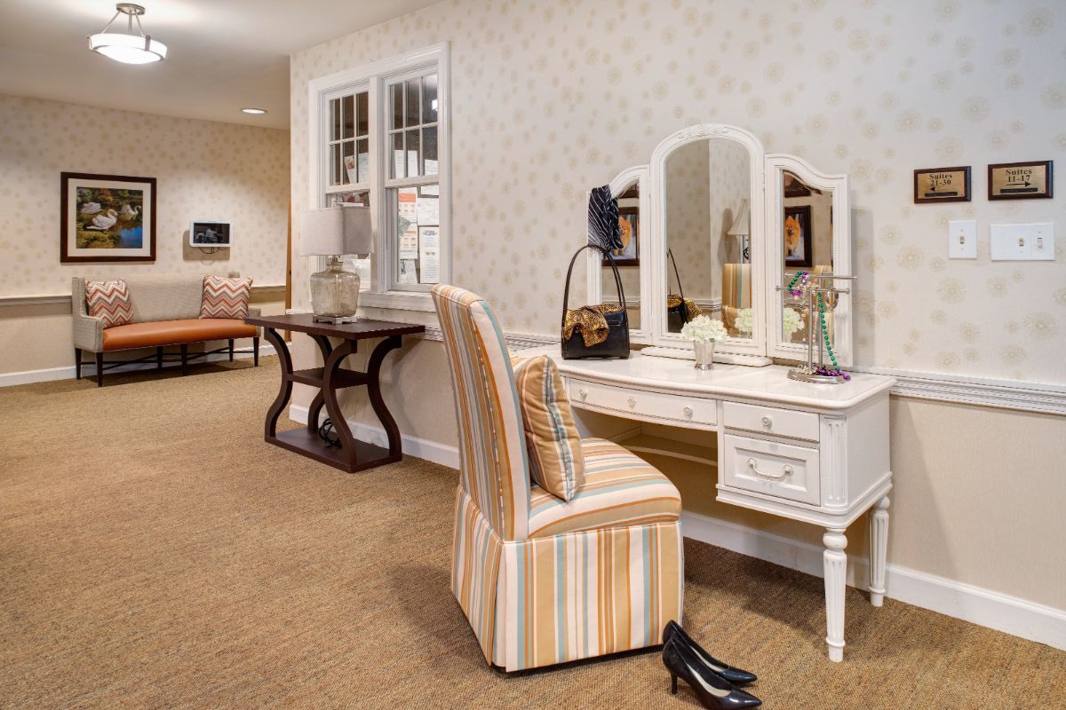 A well-appointed dressing room featuring a stylish vanity with a mirror and striped chair, complemented by elegant decor.
