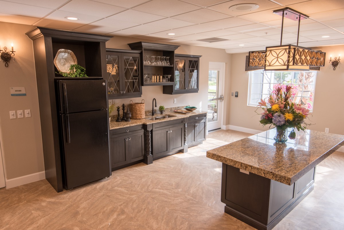 A modern kitchen interior featuring dark cabinets, a central island with flowers, and stylish lighting.