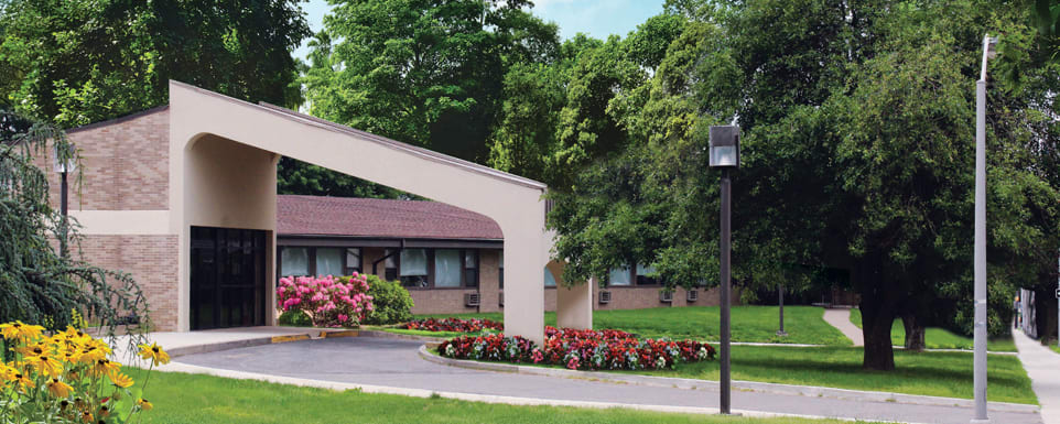 A landscaped entrance with flowers and trees in front of a building.