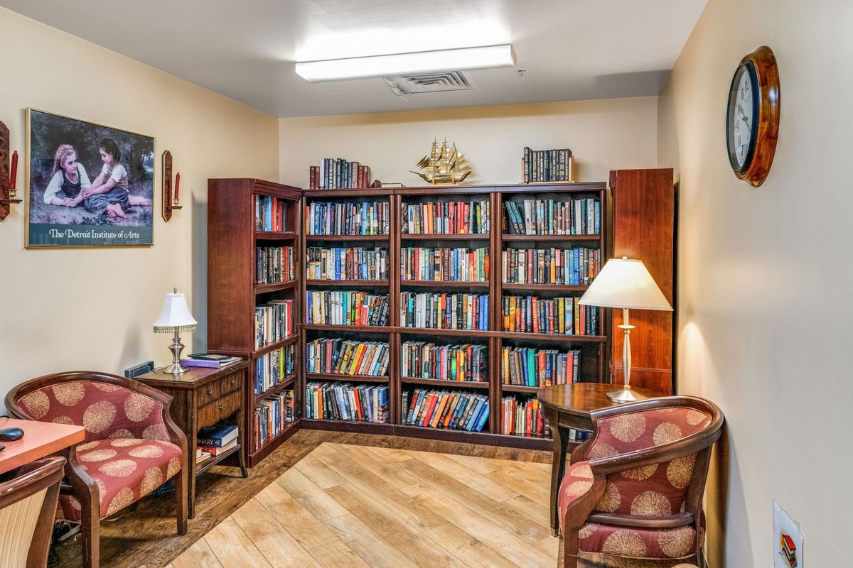 A cozy reading room with bookshelves filled with books, accompanied by comfortable chairs and a lamp.